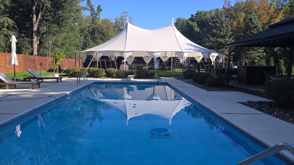 White high-peak tent reflected in a clear blue swimming pool.