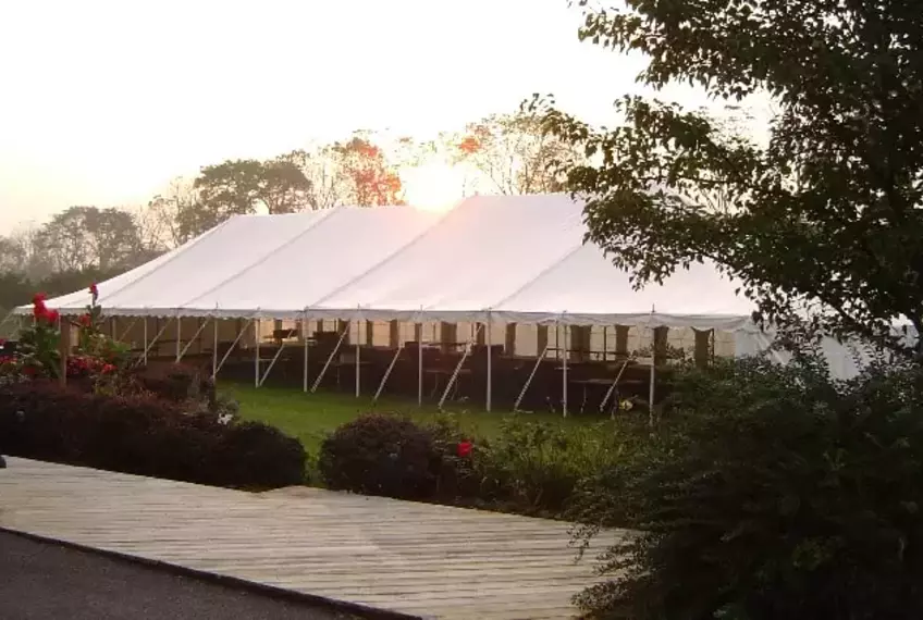 Large white pole tent set up in a scenic outdoor location, perfect for weddings, receptions, and large gatherings. Sturdy and weather-resistant event tent.