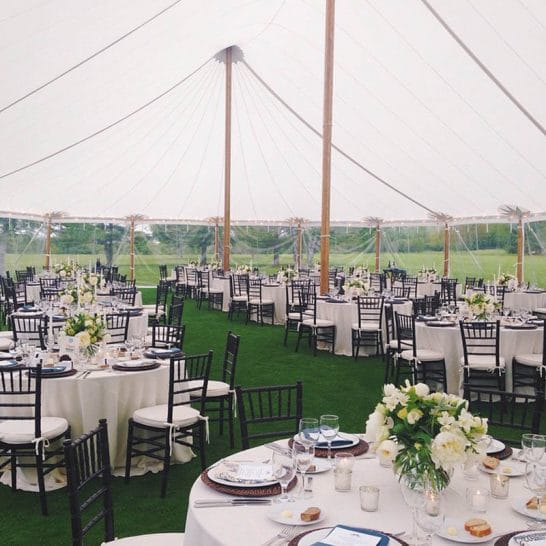 Interior of an elegant wedding tent with round tables and floral arrangements, showcasing a sophisticated event setup under a spacious pole tent.