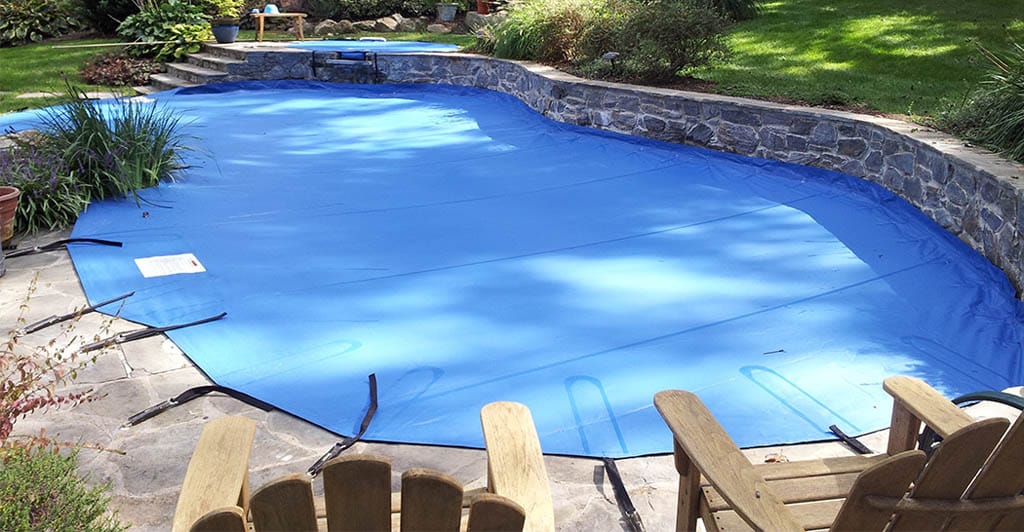 Backyard swimming pool covered with a bright blue mesh safety cover.