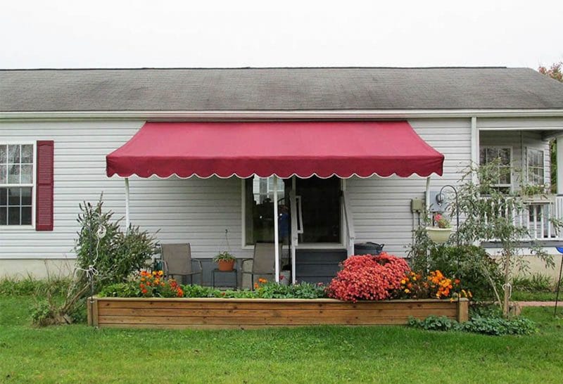 Classic residential home with a retractable burgundy awning, providing shade and enhancing curb appeal. Durable patio shade solution.