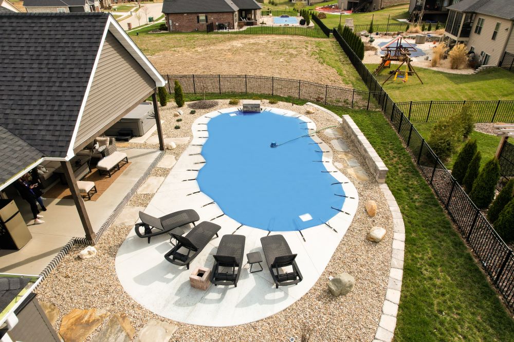 Backyard swimming pool with light blue mesh cover and surrounding lounge chairs.