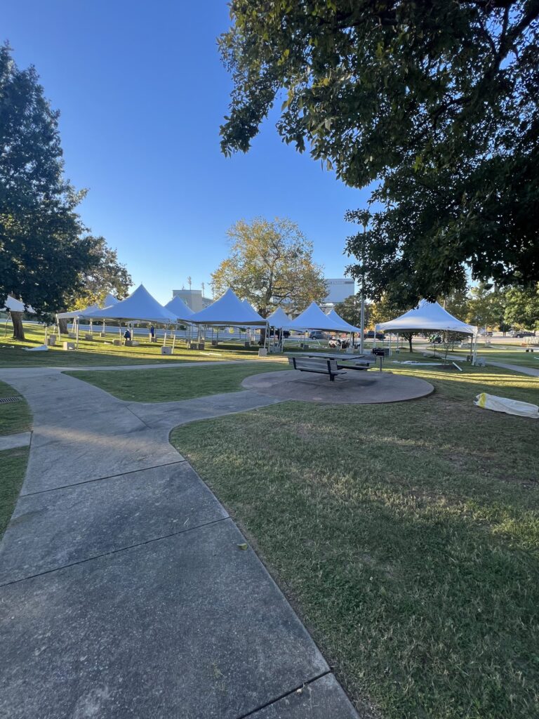 Park setting featuring multiple white event tents along a pathway.