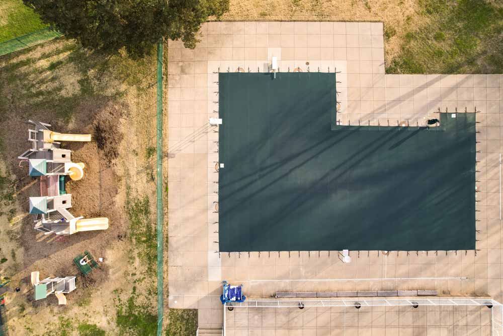 Aerial view of a square swimming pool with green mesh safety cover.