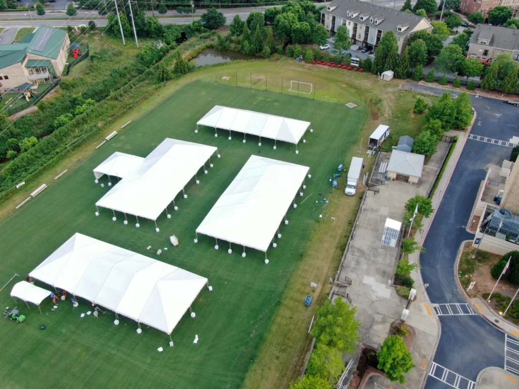 Aerial view of large white event tents set up across a green open field.
