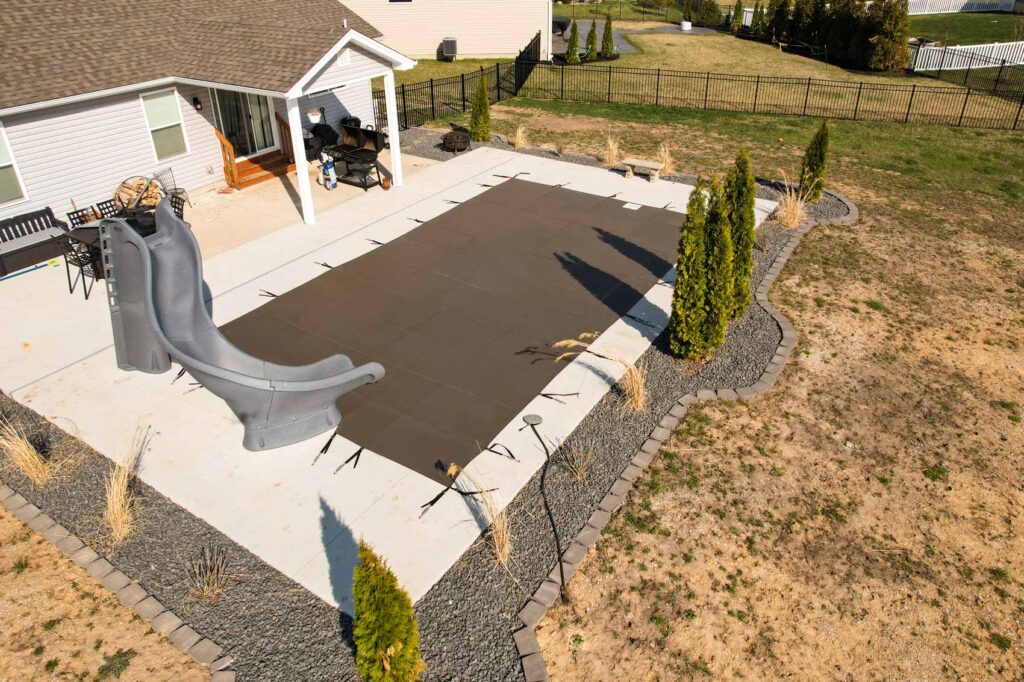 Backyard swimming pool protected by a brown mesh safety cover.