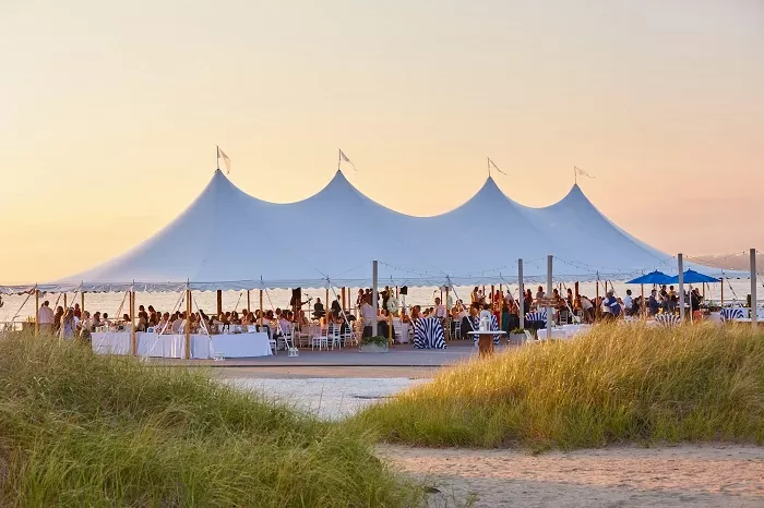 Coastal event tent at sunset with guests gathered under sailcloth peaks.