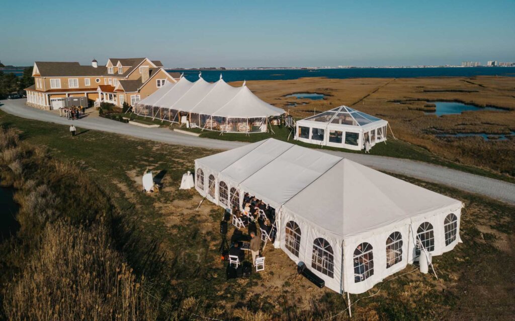 Large white event tent setup on a coastal property near the water.