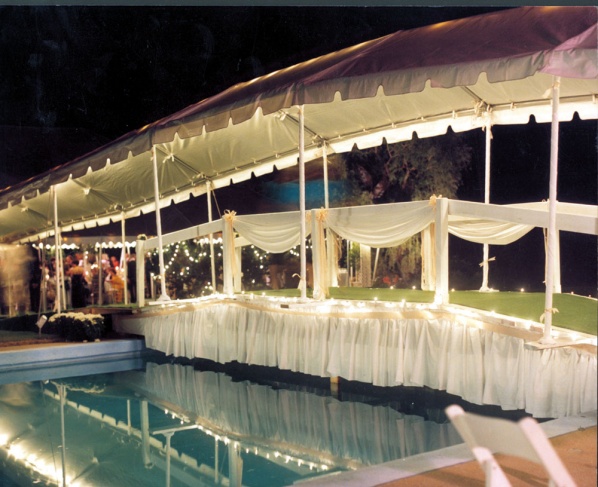 Elegant tented walkway over a pool, illuminated with string lights, creating a stunning venue for upscale outdoor events.