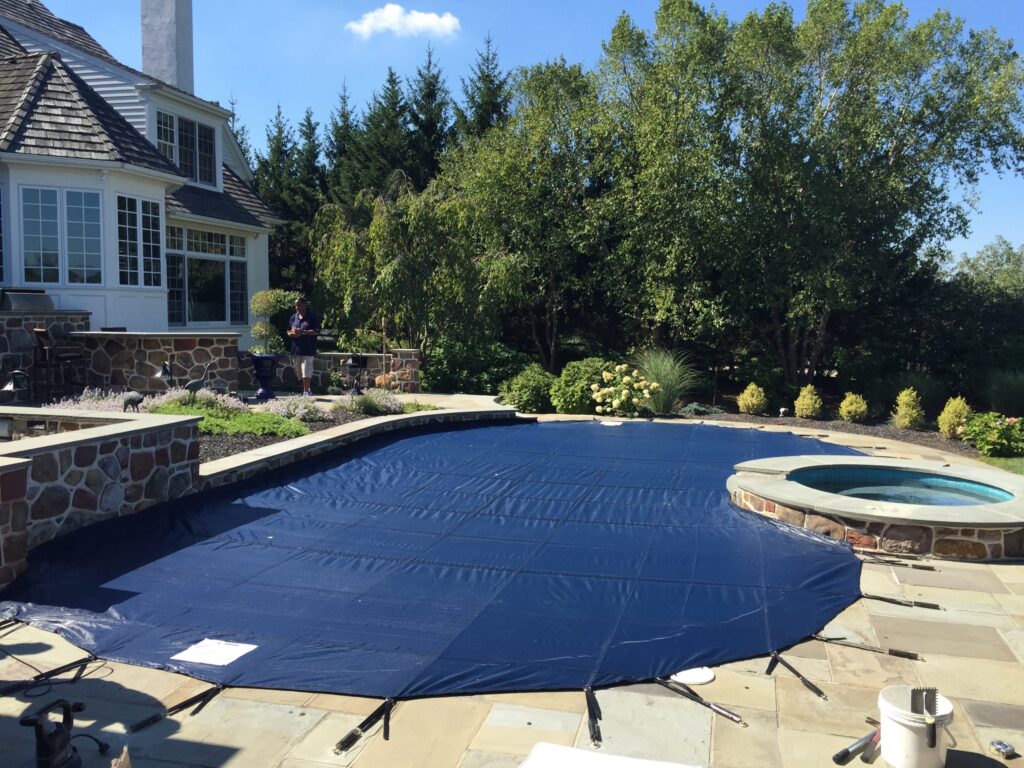 Curved swimming pool secured with a black safety cover surrounded by greenery.