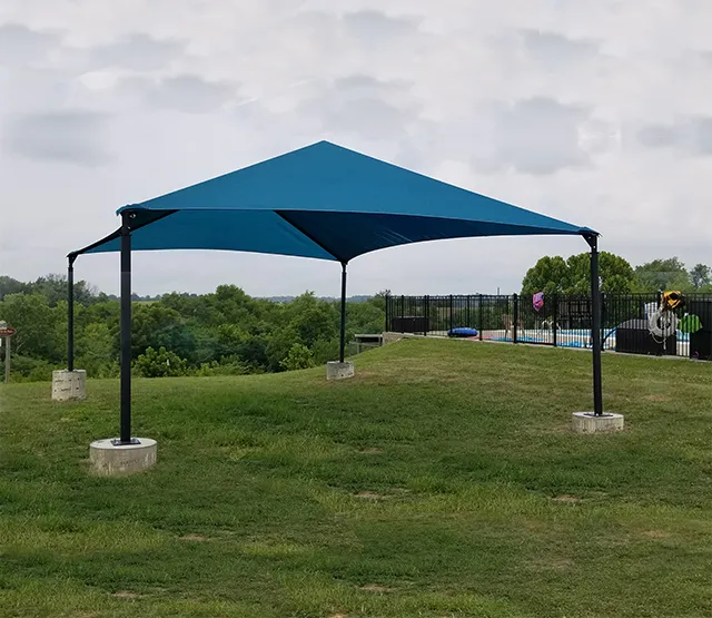 Large teal shade structure installed over a grassy recreational area.