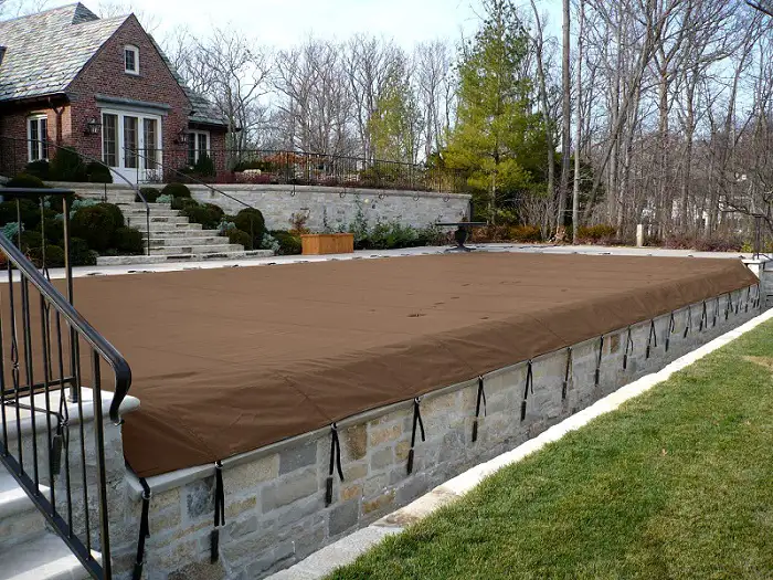 Long rectangular pool covered with a brown solid safety cover.