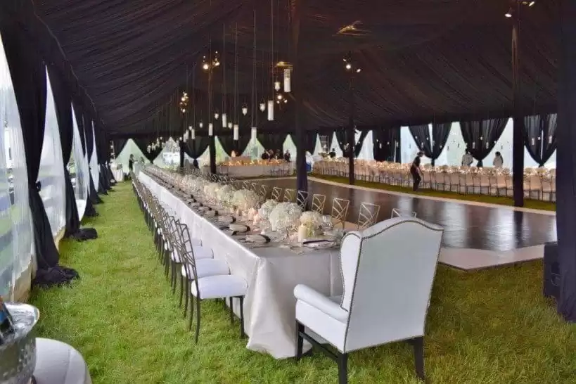 Long banquet setup inside white tent – elegant dining arrangement with chandeliers and decorated tables.