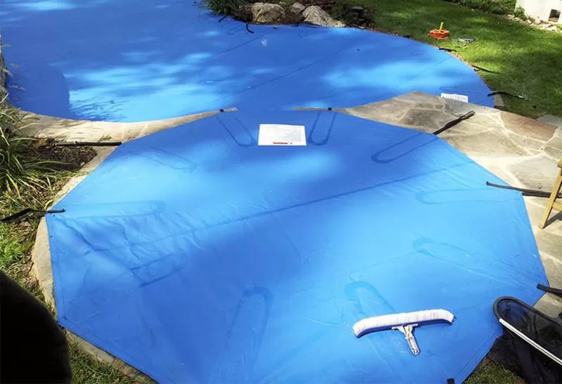 Blue pool safety cover stretched across an irregularly shaped backyard pool.