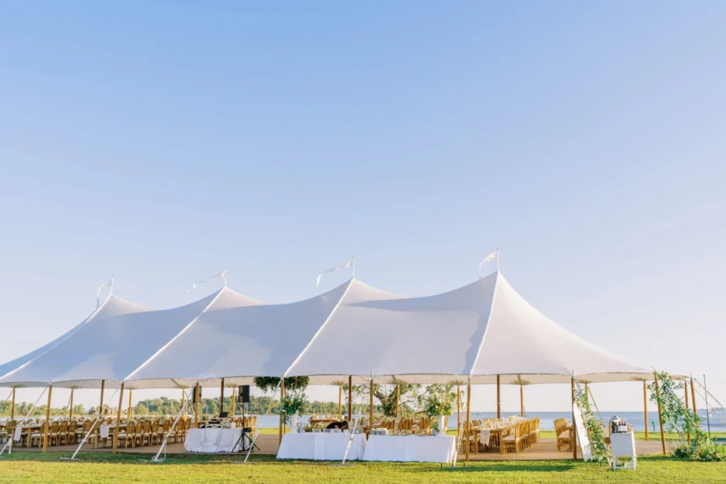 White peak-top event tent set up on grass with palm trees.