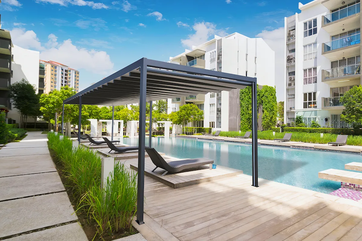 Poolside deck with dark frame louvered pergola in a residential setting.