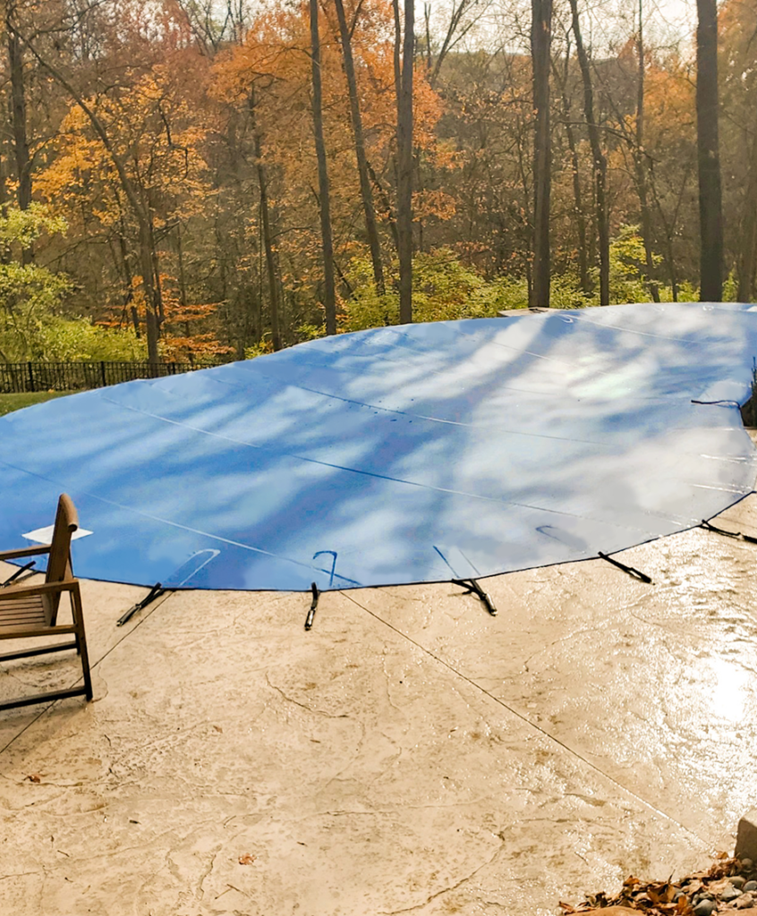 Blue pool safety cover installed on backyard pool.