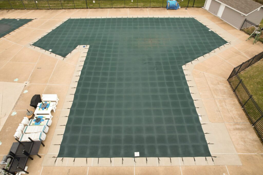 Rectangular green mesh pool cover secured over a backyard pool.