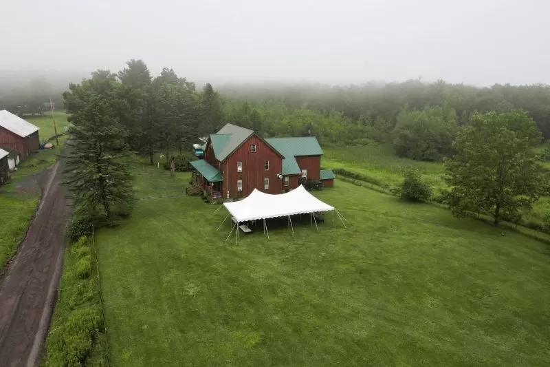 Smaller white tent beside red brick house in countryside.