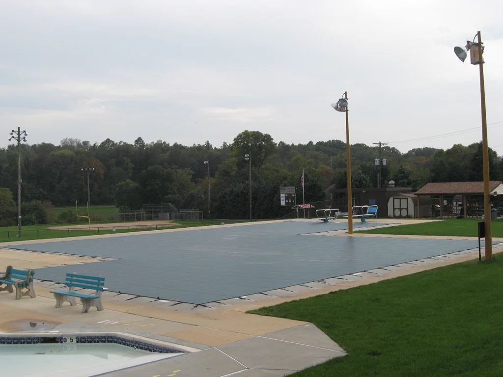 Green safety pool cover on backyard pool – Small rectangular pool secured with a green mesh cover and anchors.
