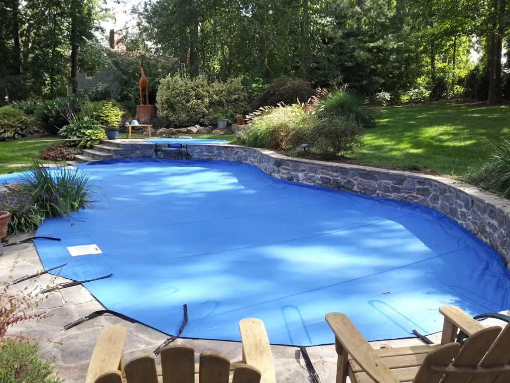 Bright blue in-ground pool with stone edging and lounge chairs nearby.