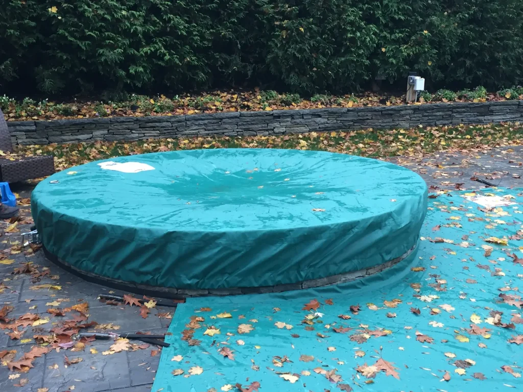 Teal round pool safety cover with leaves on surface.