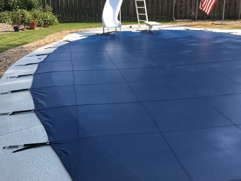Dark blue mesh pool cover stretched over inground swimming pool