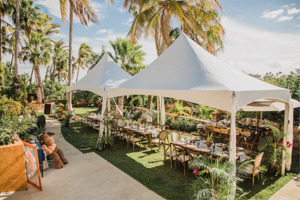 Elegant outdoor dining setup under a white canopy tent with palm trees.