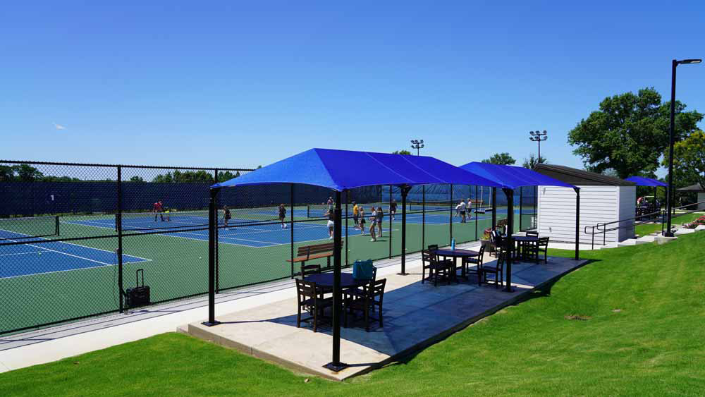 Blue canopy shade over picnic tables beside a sports field.