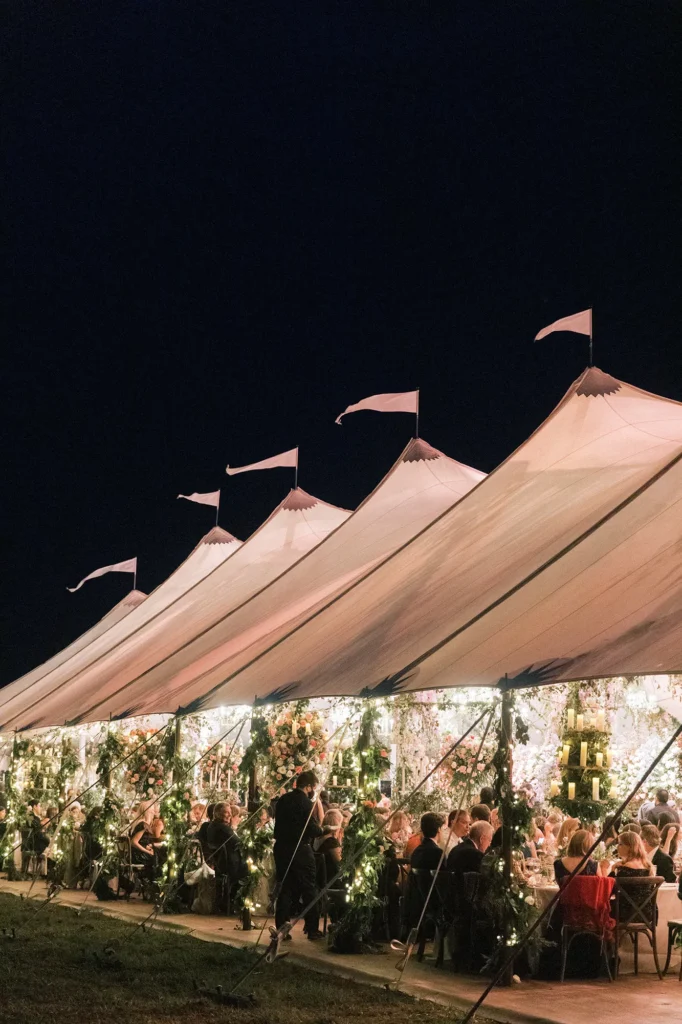 Row of peaked sailcloth tents with decorative flags at night.