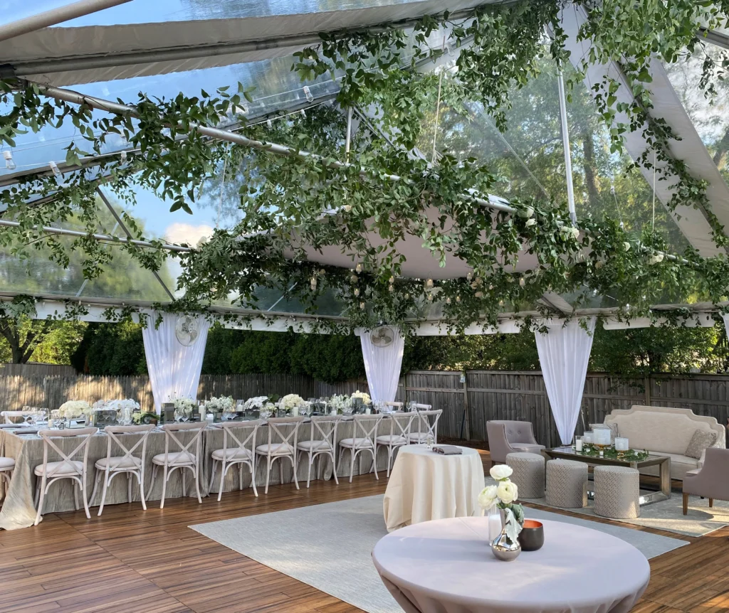 Transparent tent decorated with hanging flowers and white seating.