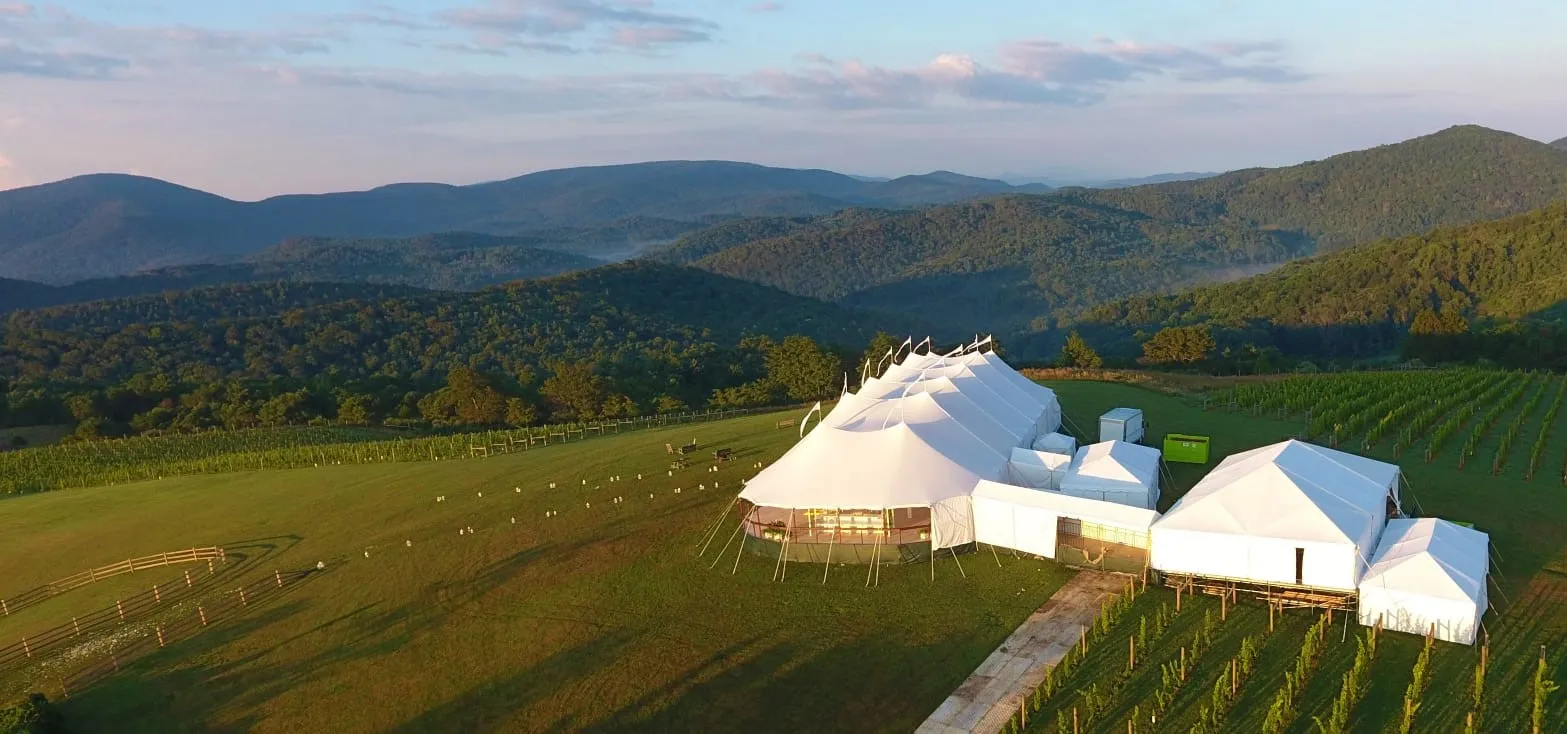 White event tent set up on a grassy hill with mountain views in the background.