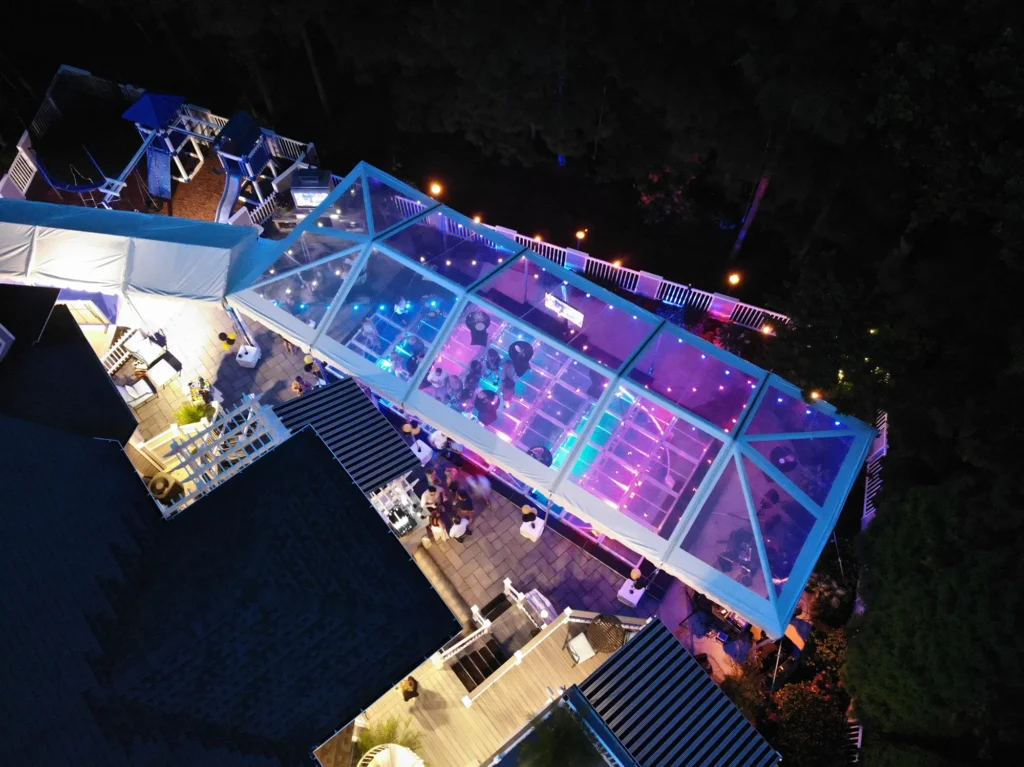 Aerial night view of a clear-top tent illuminated for an outdoor event.