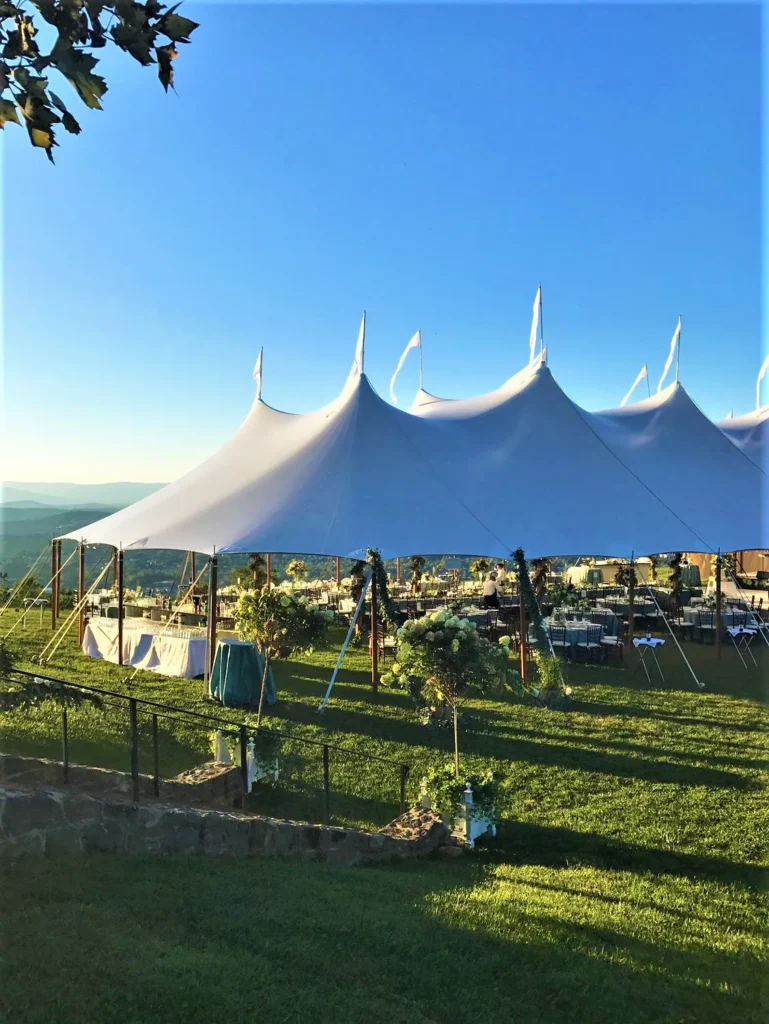 Large white sailcloth tent with peaks beside a waterfront.