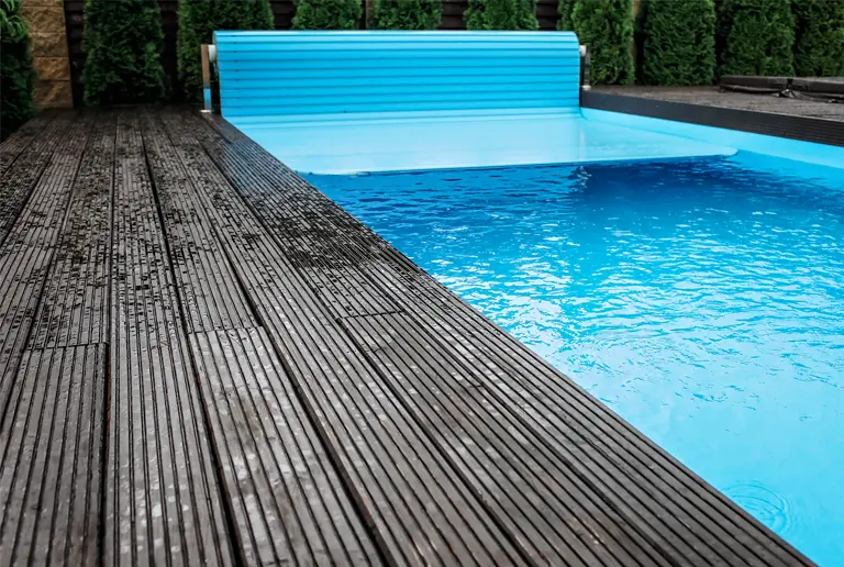 Automatic retractable blue pool cover partially rolled across inground pool