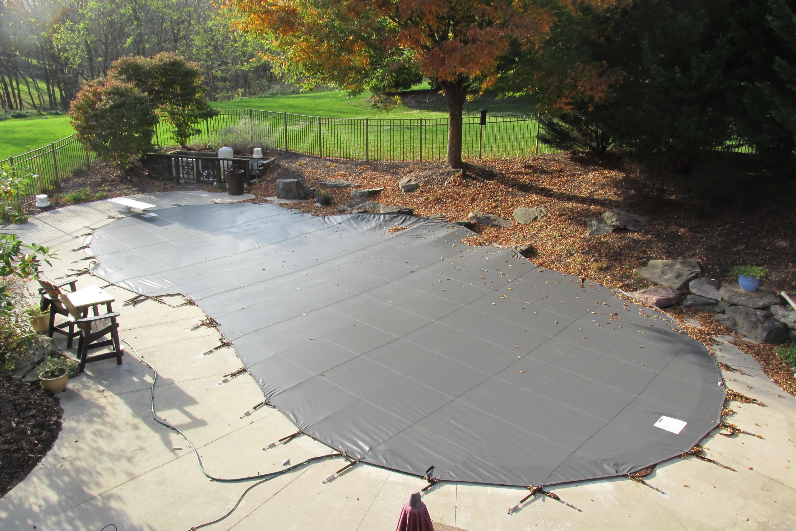 Gray rectangular pool safety cover secured around backyard pool in autumn setting