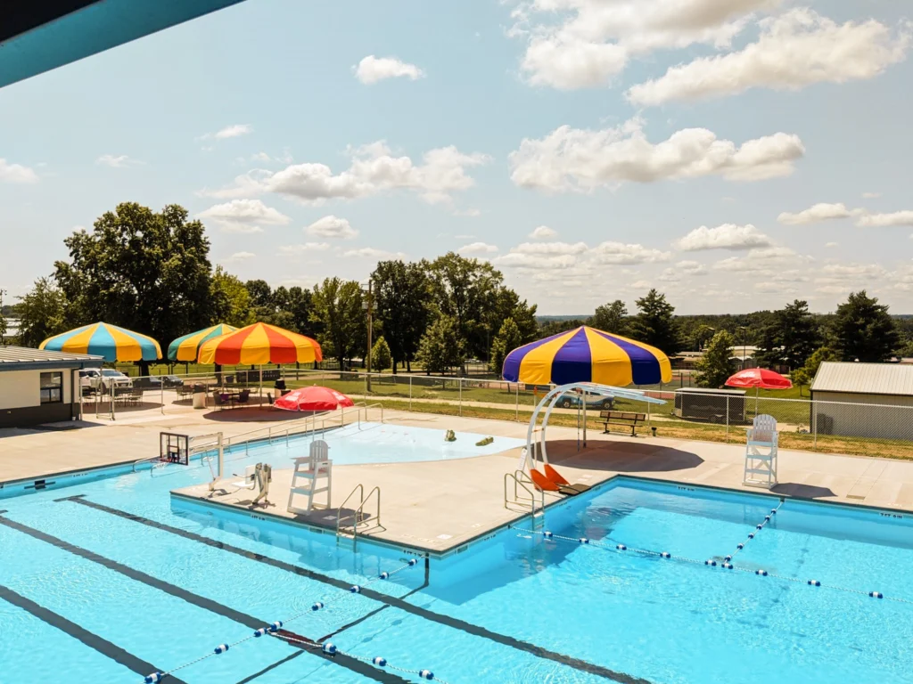 Outdoor swimming pool with colorful shade umbrellas and play structures.