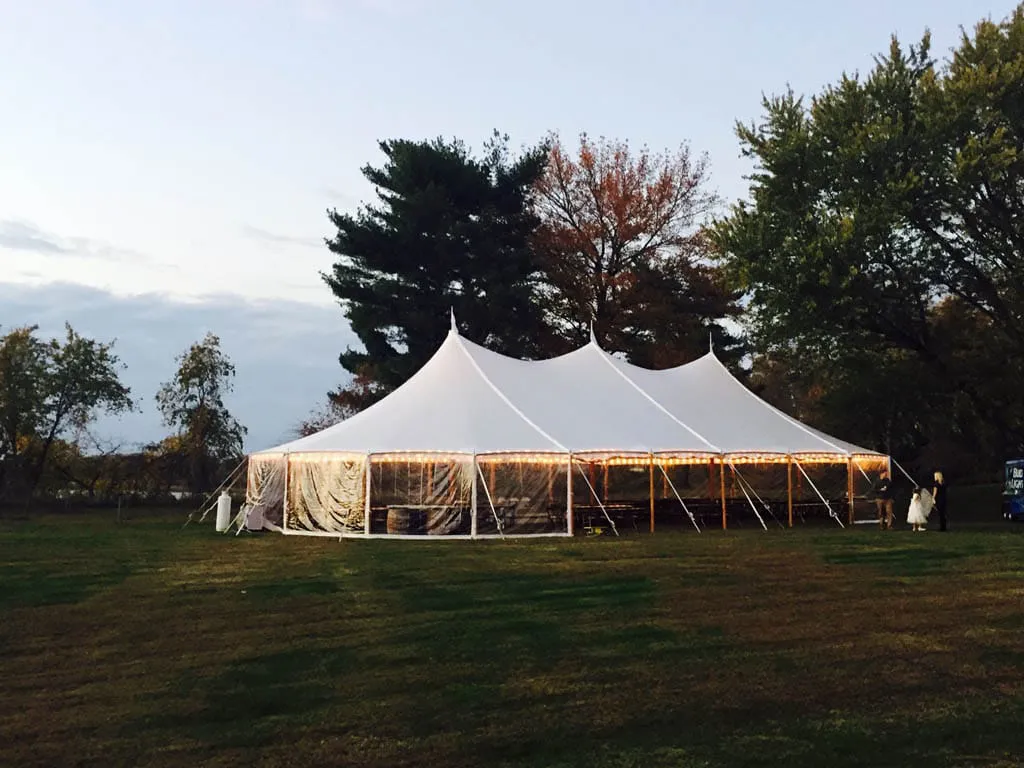 Sailcloth event tent with high xpeaks set up on a grassy field at sunset.