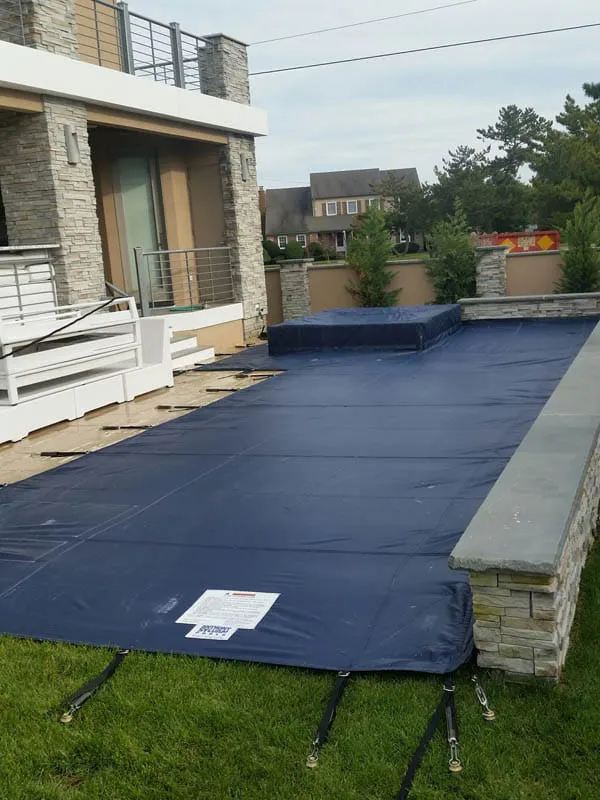 Backyard swimming pool protected with a dark blue mesh safety cover.
