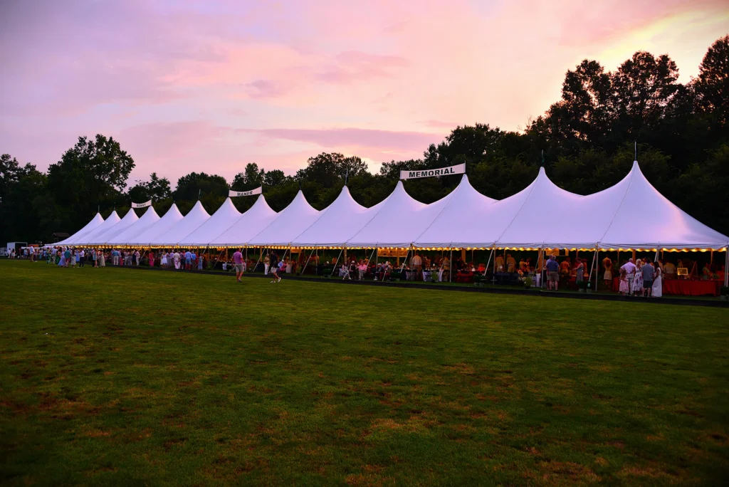 White frame tent rental setup on a grassy surface for an outdoor wedding event