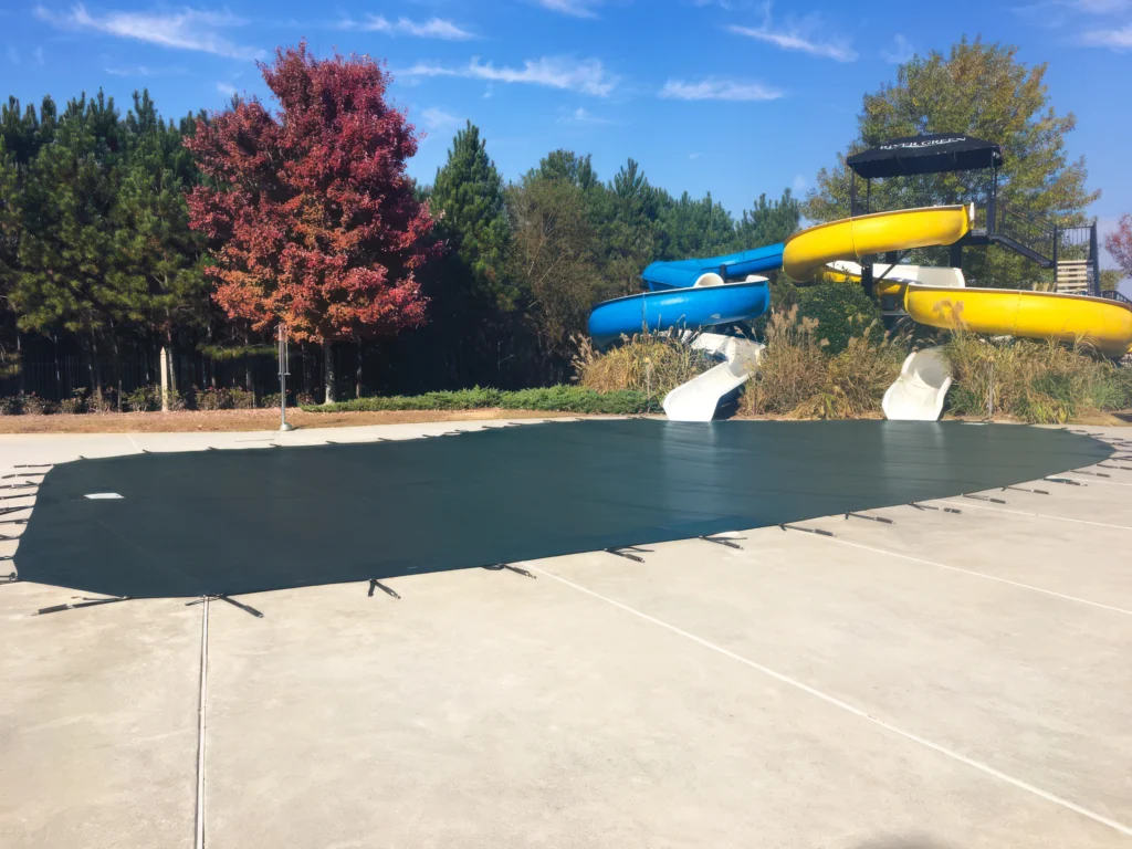 Large commercial pool covered with a tightly secured green mesh safety cover.
