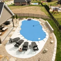 Backyard swimming pool with light blue mesh cover and surrounding lounge chairs.