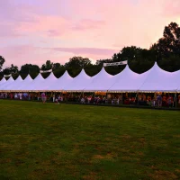 White frame tent rental setup on a grassy surface for an outdoor wedding event