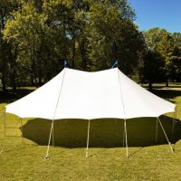 White pole tent set up on a grassy field for an outdoor gathering.